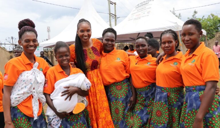 THRIVE ED Sere stands with 6 girls from a Dance+Therapy group. Sere wears a bright orange dress and the girls are wearing matching orange tops with beautiful blue, green, and orange skirts.